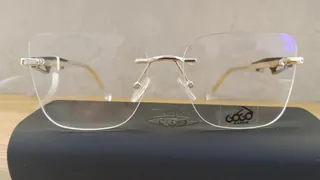 Montura de tres piezas sin aro con lentes cuadrados y puente dorado, sobre un estuche, para dama