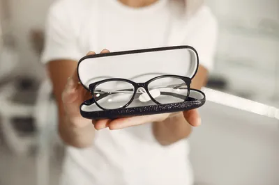 Manos que sostienen unas gafas de montura negra en su estuche abierto